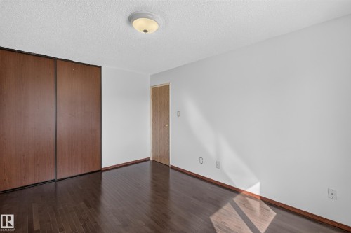 Spacious room featuring wood-finish flooring, full-height sliding closet doors, and a ceiling-mounted light fixture - 23 Willowdale Place Nw, Edmonton, AB 