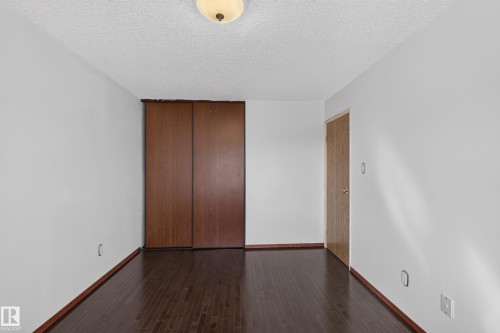 Wood-finish flooring, white painted walls, wood-finish bi-fold closet doors, and a flush mount ceiling light - 23 Willowdale Place Nw, Edmonton, AB 