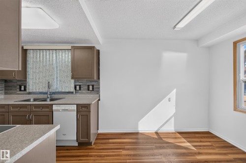 Kitchen featuring wood-finish flooring, brown cabinetry, a tile backsplash, and a double basin sink with a single-handle faucet - 23 Willowdale Place Nw, Edmonton, AB 