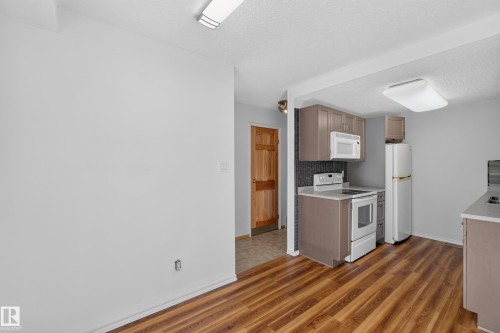 Kitchen featuring wood-finish flooring, brown cabinetry, white appliances, and a dark tile backsplash - 23 Willowdale Place Nw, Edmonton, AB 