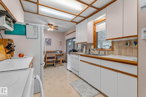 White cabinetry with wood-finish trim, ceramic tile backsplash, dual basin stainless steel sink, and a multi-pane window - 13432 134 Street Nw, Edmonton, AB - Indoor