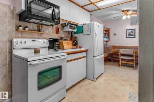 White kitchen appliances including a range and refrigerator, light wood-finish countertops, white cabinetry, and tan tiled backsplash - 13432 134 Street Nw, Edmonton, AB - Indoor Photo Showing Kitchen