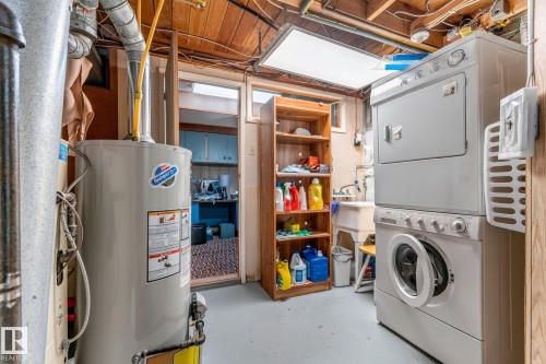 Utility area featuring a water heater, stacked washer and dryer, laundry sink, and wood-finish shelving - 13432 134 Street Nw, Edmonton, AB - Indoor Photo Showing Laundry Room