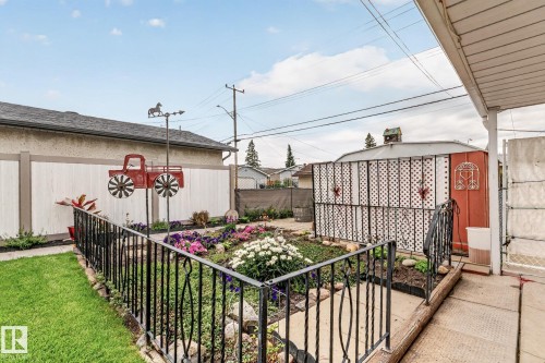 Manicured lawn, wrought iron garden fence, concrete patio, garden bed with varied plantings, and a privacy fence - 13432 134 Street Nw, Edmonton, AB - Outdoor With Deck Patio Veranda