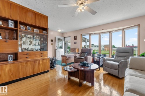 Expansive bay window, wood-finish flooring, built-in display cabinetry, ceiling fan, and paneled entry door - 13432 134 Street Nw, Edmonton, AB - Indoor Photo Showing Living Room
