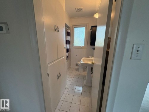 Built-in storage cabinetry, pedestal sink, wall-mounted light fixture, and tiled flooring - 9733 143 Street Nw, Edmonton, AB - Indoor