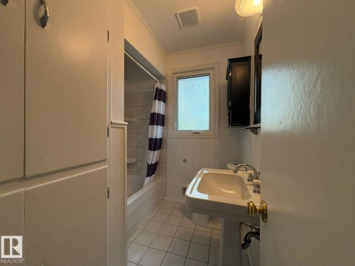 Pedestal sink, wall-mounted medicine cabinet, integrated bathtub and shower, tiled flooring, and built-in storage cabinetry - 9733 143 Street Nw, Edmonton, AB - Indoor Photo Showing Bathroom