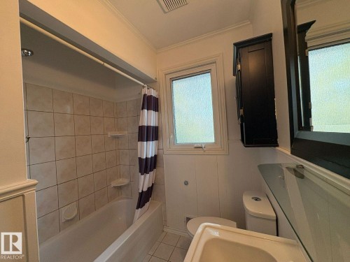 Built-in bathtub with tiled surround, paneled wall detailing, window with frosted glass, wall-mounted storage cabinet, and vanity with integrated sink - 9733 143 Street Nw, Edmonton, AB - Indoor Photo Showing Bathroom
