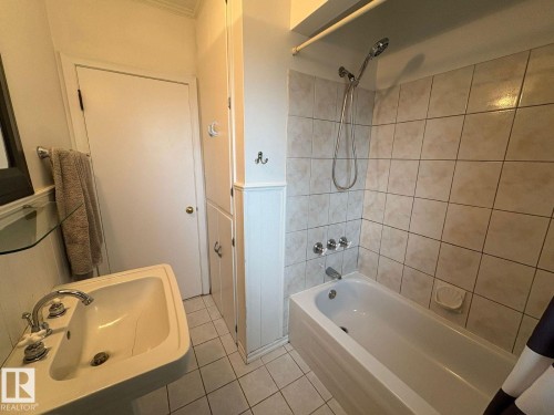 Pedestal sink with chrome fixtures, built-in storage cabinetry, white subway tile tub surround, and tiled flooring - 9733 143 Street Nw, Edmonton, AB - Indoor Photo Showing Bathroom