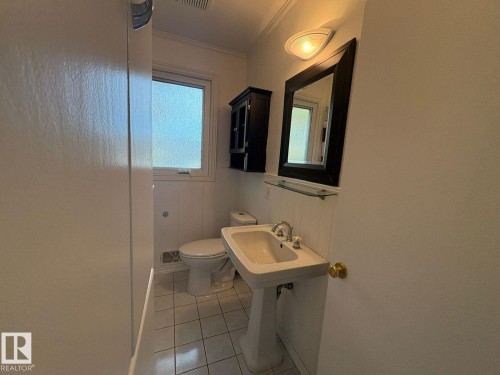 Pedestal sink with chrome fixtures, framed mirror, wall-mounted light fixture, and tiled flooring - 9733 143 Street Nw, Edmonton, AB - Indoor Photo Showing Bathroom
