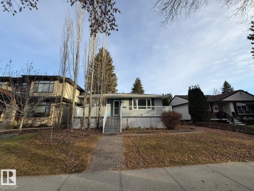 Single-story residence featuring a front deck with white railings, a front entrance with a light blue door, and a brick paver walkway - 9733 143 Street Nw, Edmonton, AB - Outdoor