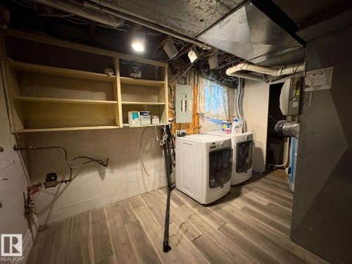Wood-finish flooring with a durable concrete wall, exposed overhead ductwork, and built-in shelving - 9733 143 Street Nw, Edmonton, AB - Indoor Photo Showing Laundry Room