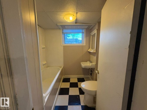 Checkered floor tile, built-in bathtub, pedestal sink, wall-mounted mirrored cabinet, and flush-mount ceiling light - 9733 143 Street Nw, Edmonton, AB - Indoor Photo Showing Bathroom
