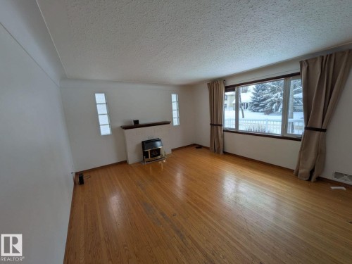 Spacious living area showcasing warm wood-finish flooring, large multi-pane windows with natural light, and neutral walls providing a blank canvas for décor - 9733 143 Street Nw, Edmonton, AB - Indoor