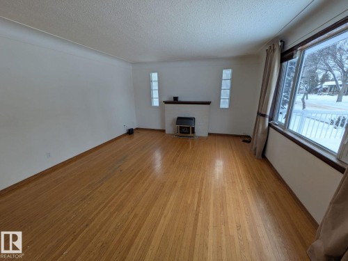 Wood-finish flooring, white walls, and a fireplace with a white mantel and dark hearth - 9733 143 Street Nw, Edmonton, AB - Indoor