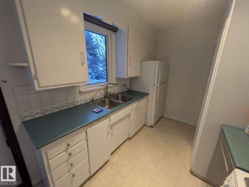 Kitchen featuring white cabinetry, dual basin stainless steel sink, and light-colored flooring - 9733 143 Street Nw, Edmonton, AB - Indoor Photo Showing Kitchen With Double Sink