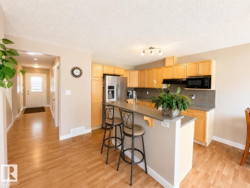 Kitchen featuring wood-finish flooring, light wood cabinetry, stainless steel refrigerator, and track lighting - 21207 90 Ave Nw, Edmonton, AB - Indoor Photo Showing Kitchen