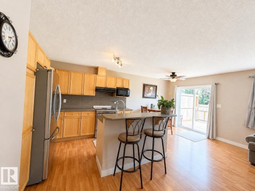 Open-concept kitchen with wood-finish flooring, stainless steel refrigerator, built-in microwave, and track lighting - 21207 90 Ave Nw, Edmonton, AB - Indoor Photo Showing Kitchen