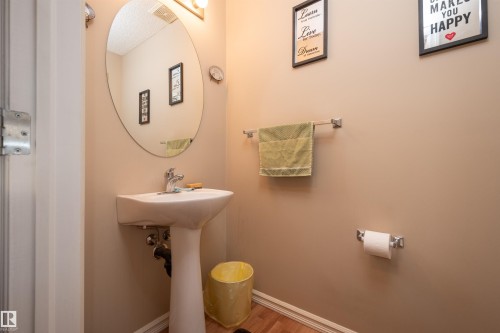 Pedestal sink with chrome faucet, oval mirror, and wood-finish flooring - 21207 90 Ave Nw, Edmonton, AB - Indoor Photo Showing Bathroom