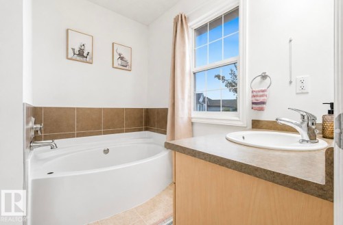Corner soaking tub with tile surround, single-pane window, vanity with integrated sink, and chrome fixtures - 21207 90 Ave Nw, Edmonton, AB - Indoor Photo Showing Bathroom