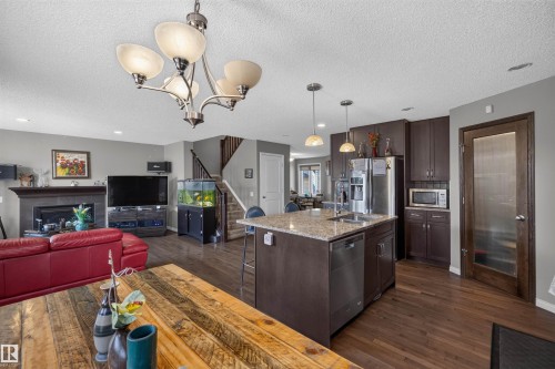 Open-concept living space featuring wood-finish flooring, a kitchen island with granite-style countertop, dark wood cabinetry, and stainless steel appliances - 16515 139 Street Nw, Edmonton, AB - Indoor With Fireplace