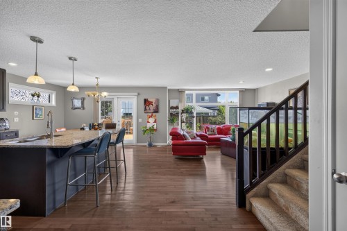 Open-concept living area with wood-finish flooring, a kitchen island with stone countertops, pendant lighting, and a sliding glass door to the exterior - 16515 139 Street Nw, Edmonton, AB - Indoor Photo Showing Kitchen With Upgraded Kitchen