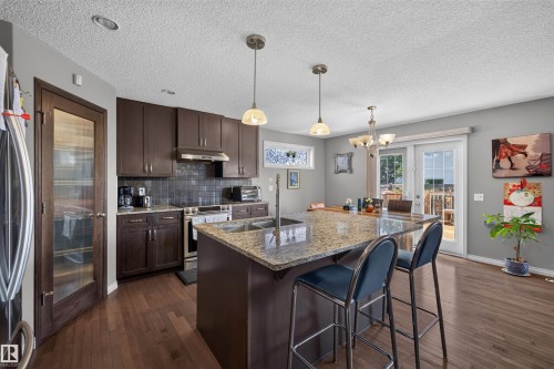 Kitchen featuring dark wood-finish cabinetry, stainless steel appliances, and a central island with a granite countertop and integrated sink - 16515 139 Street Nw, Edmonton, AB - Indoor Photo Showing Kitchen With Double Sink With Upgraded Kitchen