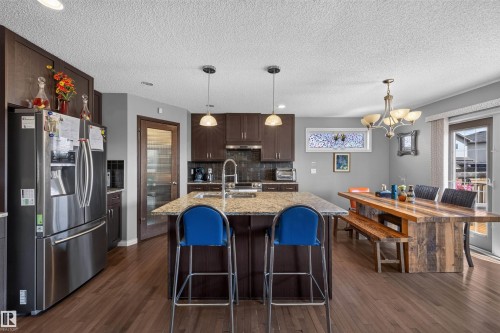 Kitchen featuring wood-finish flooring, dark wood cabinetry, a granite-topped island with dual pendant lighting, and stainless steel appliances - 16515 139 Street Nw, Edmonton, AB - Indoor Photo Showing Kitchen With Upgraded Kitchen