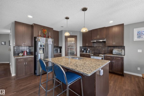 Kitchen featuring dark wood cabinetry, stainless steel appliances, granite countertops, and wood-finish flooring - 16515 139 Street Nw, Edmonton, AB - Indoor Photo Showing Kitchen With Double Sink With Upgraded Kitchen