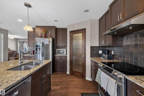 Kitchen featuring granite countertops, wood-finish flooring, dark wood cabinetry, a double basin sink, and stainless steel appliances - 16515 139 Street Nw, Edmonton, AB - Indoor Photo Showing Kitchen With Double Sink With Upgraded Kitchen