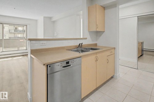 Kitchen featuring a stainless steel dishwasher, double basin sink, light wood-finish cabinetry, and a pass-through counter with a tiled backsplash - #226 17011 67 Av Nw, Edmonton, AB - Indoor Photo Showing Kitchen With Double Sink
