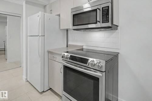 White cabinetry, stainless steel range, built-in microwave, subway tile backsplash, and light-toned countertops - #226 17011 67 Av Nw, Edmonton, AB - Indoor Photo Showing Kitchen