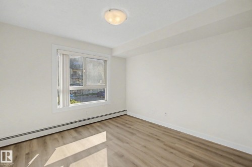 Wood-finish flooring, white walls, and a prominent window with white trim - #226 17011 67 Av Nw, Edmonton, AB - Indoor Photo Showing Other Room