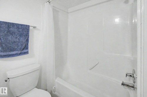 White toilet with chrome flush lever, adjacent to a shower-tub combination with a white surround and chrome fixtures - #226 17011 67 Av Nw, Edmonton, AB - Indoor Photo Showing Bathroom