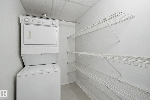 Laundry area featuring a stacked washer and dryer, wire shelving, and a hanging rod - #226 17011 67 Av Nw, Edmonton, AB - Indoor Photo Showing Laundry Room