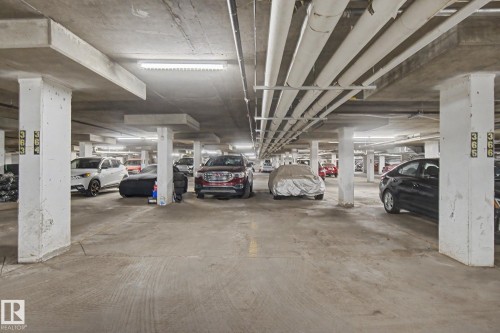 Concrete parking structure featuring overhead lighting and exposed utility pipes - #226 17011 67 Av Nw, Edmonton, AB - Indoor Photo Showing Garage