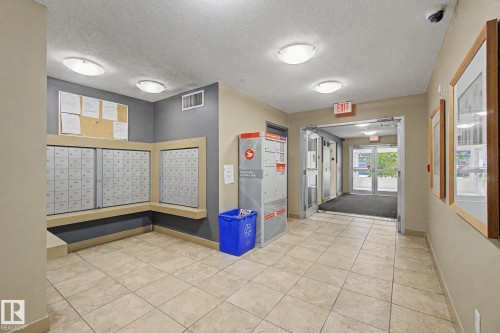 Tiled flooring throughout the entrance, featuring recessed ceiling lighting, a security camera, and a glass-paneled exit door - #226 17011 67 Av Nw, Edmonton, AB - Indoor Photo Showing Other Room