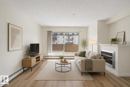 Living area with wood-finish flooring, a built-in fireplace, and a large window - #226 17011 67 Av Nw, Edmonton, AB - Indoor Photo Showing Living Room With Fireplace