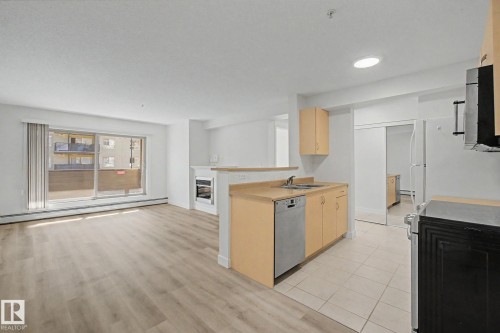 Open-concept living area with wood-finish flooring, sliding glass patio door, and integrated kitchen - #226 17011 67 Av Nw, Edmonton, AB - Indoor With Fireplace