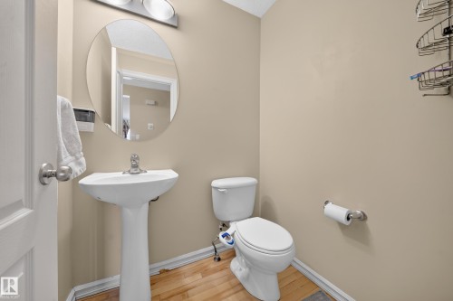 Pedestal sink with an oval mirror, overhead vanity lighting, and wood-finish flooring - 2518 33A Avenue Nw, Edmonton, AB - Indoor Photo Showing Bathroom