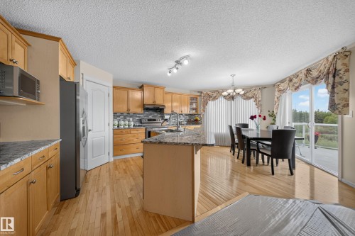 Hardwood flooring, light wood cabinetry, granite countertops, tile backsplash, and sliding glass doors with balcony access - 2518 33A Avenue Nw, Edmonton, AB - Indoor Photo Showing Kitchen