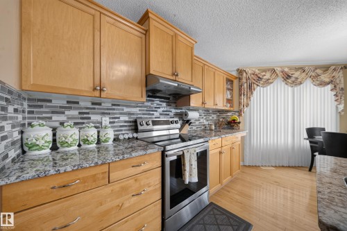 Light wood cabinetry, patterned tile backsplash, stainless steel range, and stone-finish countertops - 2518 33A Avenue Nw, Edmonton, AB - Indoor Photo Showing Kitchen