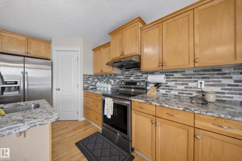 Light wood cabinetry with chrome hardware, stone countertops, stainless steel appliances, and a mosaic tile backsplash - 2518 33A Avenue Nw, Edmonton, AB - Indoor Photo Showing Kitchen With Upgraded Kitchen