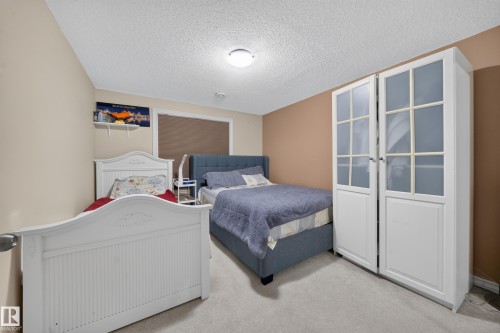 Recessed lighting, textured ceiling, light-colored carpeting, window with blinds, and a built-in wardrobe with glass-paneled doors - 2518 33A Avenue Nw, Edmonton, AB - Indoor Photo Showing Bedroom