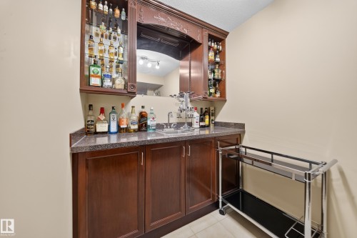 Built-in wet bar with wood cabinetry, a sink with a stainless steel faucet, and a stone-look countertop - 2518 33A Avenue Nw, Edmonton, AB - Indoor