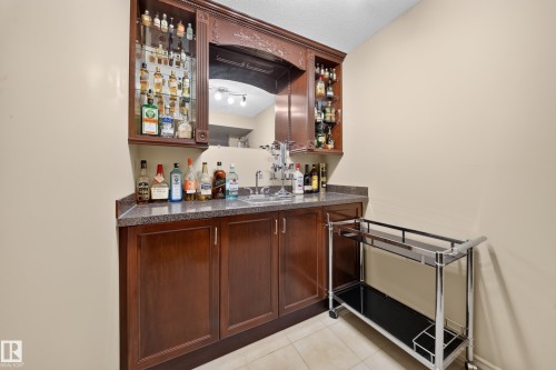 Built-in wet bar featuring a polished countertop, undermount sink, dark wood cabinetry, and a mirrored backsplash - 2518 33A Avenue Nw, Edmonton, AB - Indoor