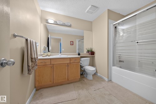 Wood-finish vanity with an integrated sink, large wall-mounted mirror, three-light vanity fixture, and a shower-tub combination with sliding glass doors - 2518 33A Avenue Nw, Edmonton, AB - Indoor Photo Showing Bathroom