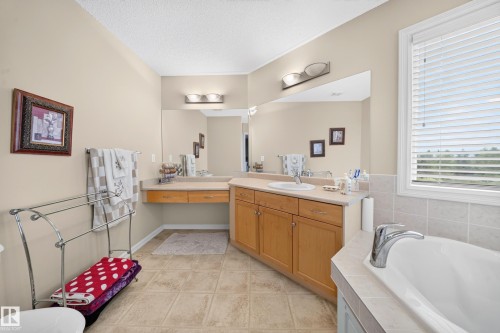 Full-length vanity mirror, wood-finish cabinetry, tile flooring, built-in bathtub, and window with blinds - 2518 33A Avenue Nw, Edmonton, AB - Indoor Photo Showing Bathroom
