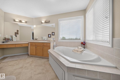 Corner soaking tub with tiled surround, light wood-finish vanity cabinetry, dual vanity mirrors, and tiled flooring - 2518 33A Avenue Nw, Edmonton, AB - Indoor Photo Showing Bathroom