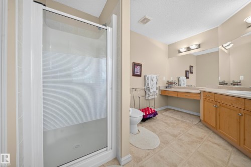Tiled flooring, dual vanity with integrated sinks, wood-finish cabinetry, and a shower with a frosted glass enclosure - 2518 33A Avenue Nw, Edmonton, AB - Indoor Photo Showing Bathroom